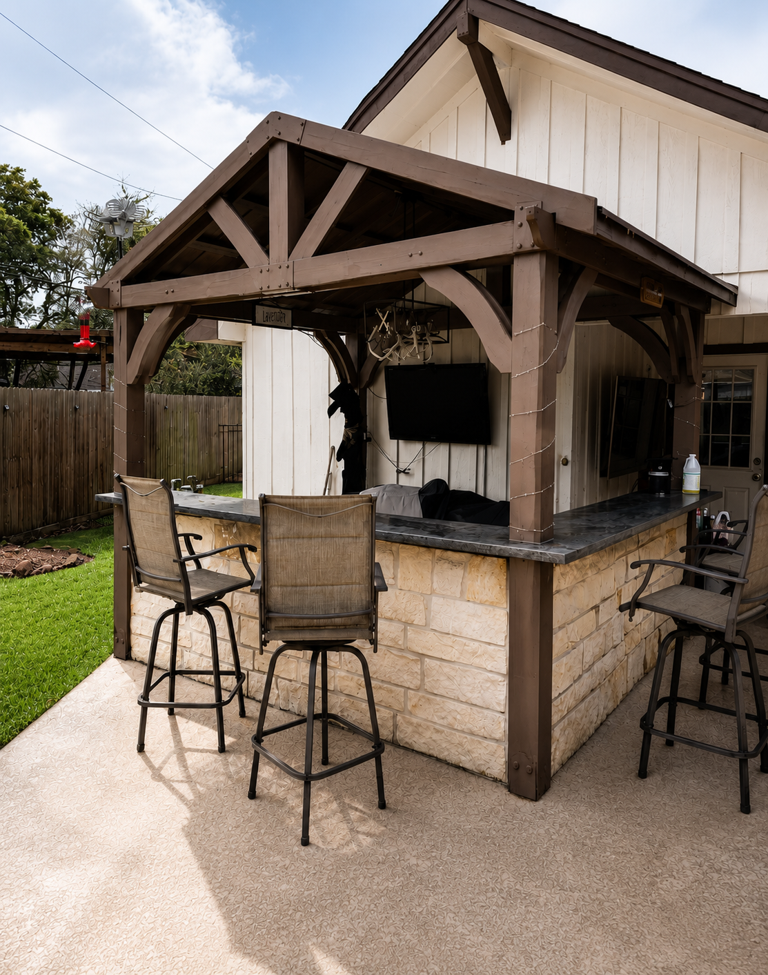 Custom outdoor living space featuring a timber-frame covered patio bar with stone veneer, granite countertops, bar seating, and an outdoor entertainment area built by Mason's Quality Construction